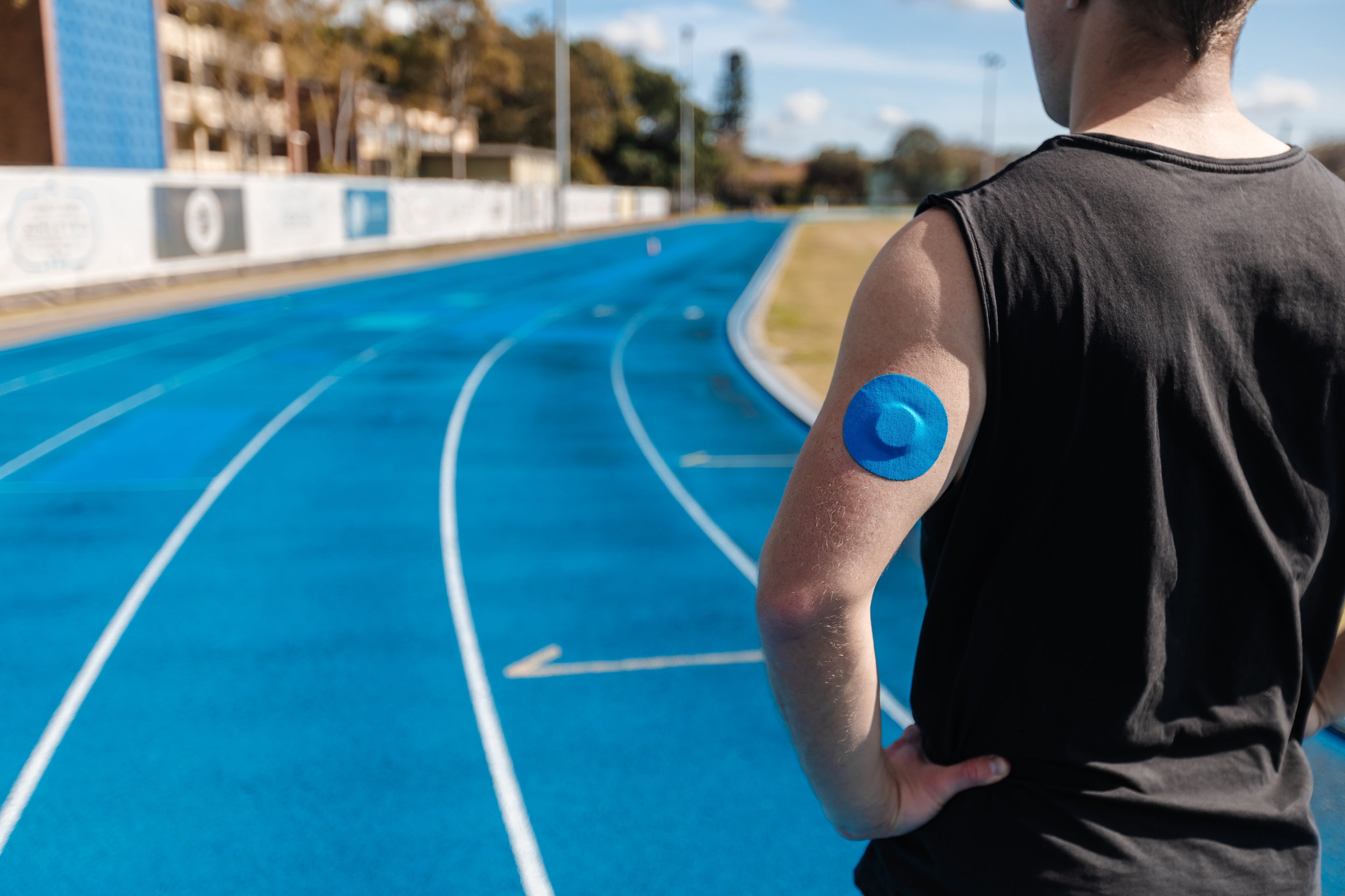 Ryan on running track with cgm patches attached in back of the arm